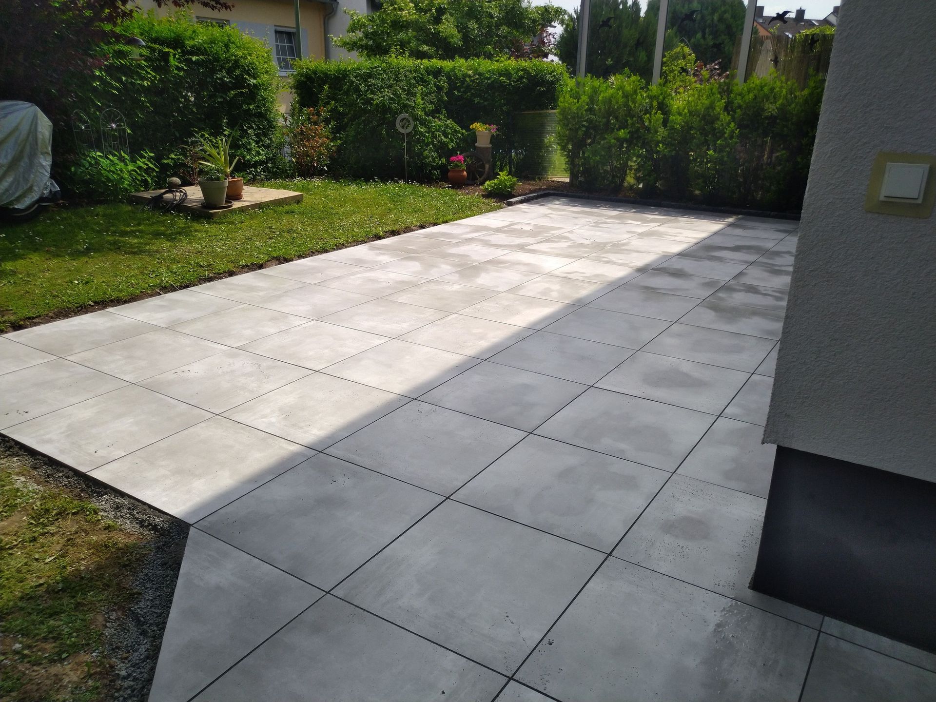 Grau geflieste Terrasse in einem Hinterhof mit Gras und Grün.