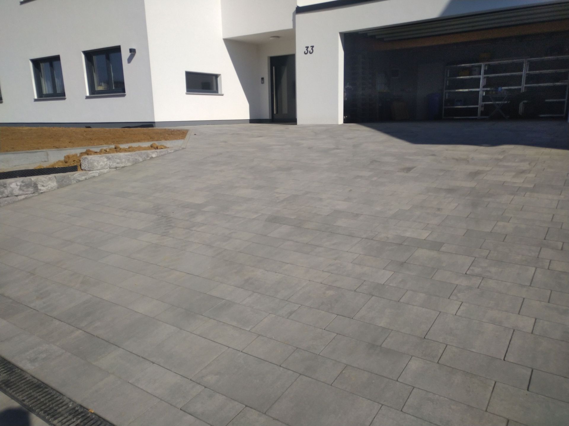 Grau gepflasterte Auffahrt, die zu einem modernen weißen Haus mit Carport führt.