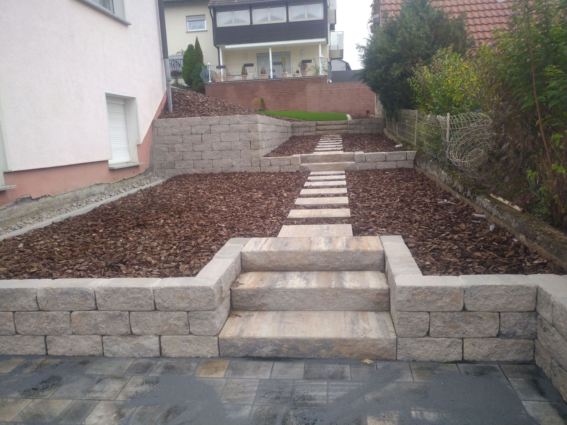 Steinstufen und Stützmauern in einem angelegten Garten, die zu einem Haus führen.