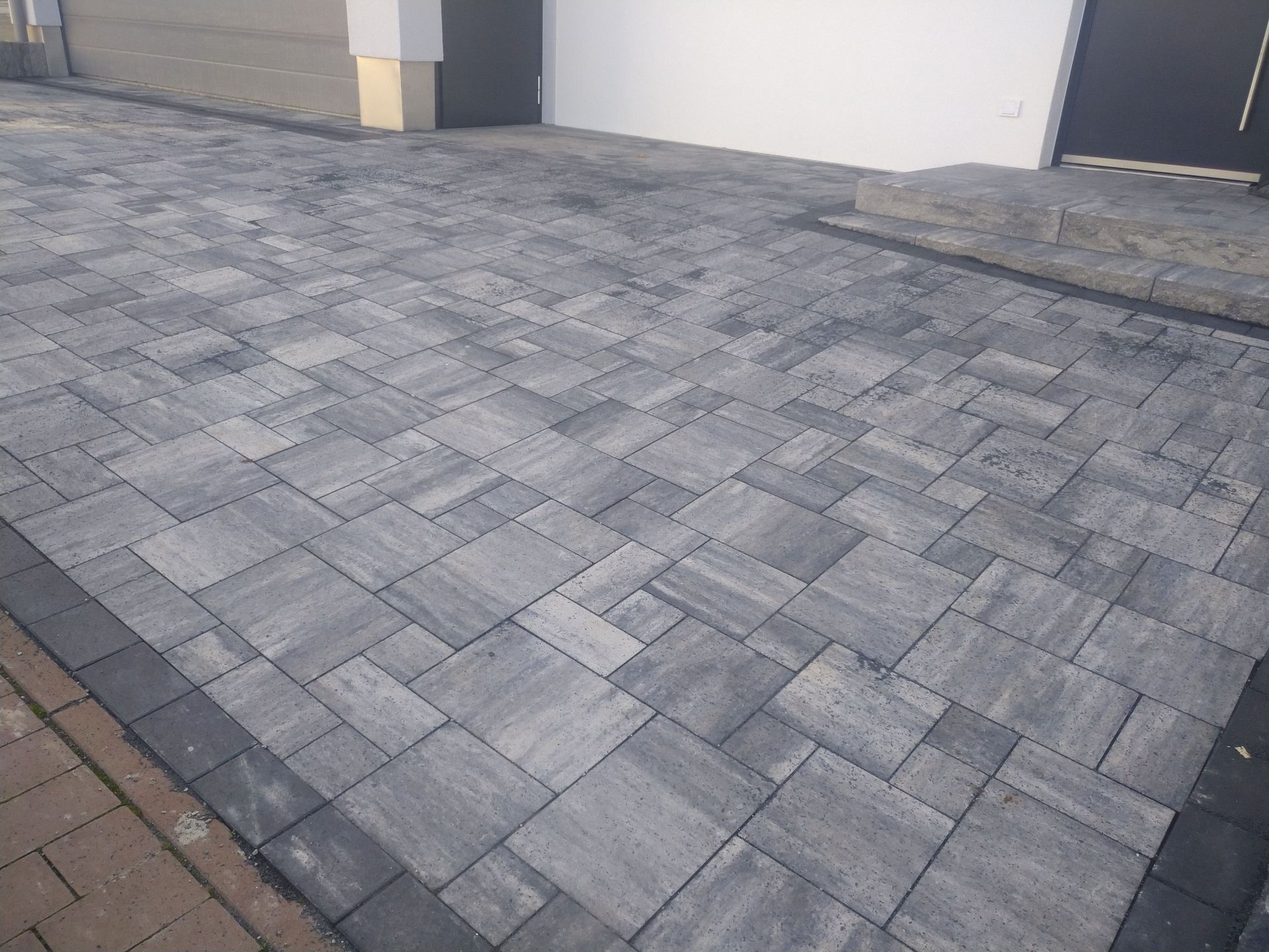 Graue Pflastersteine ​​bilden eine Auffahrt, die zu einer weißen Wand und einer Tür führt.