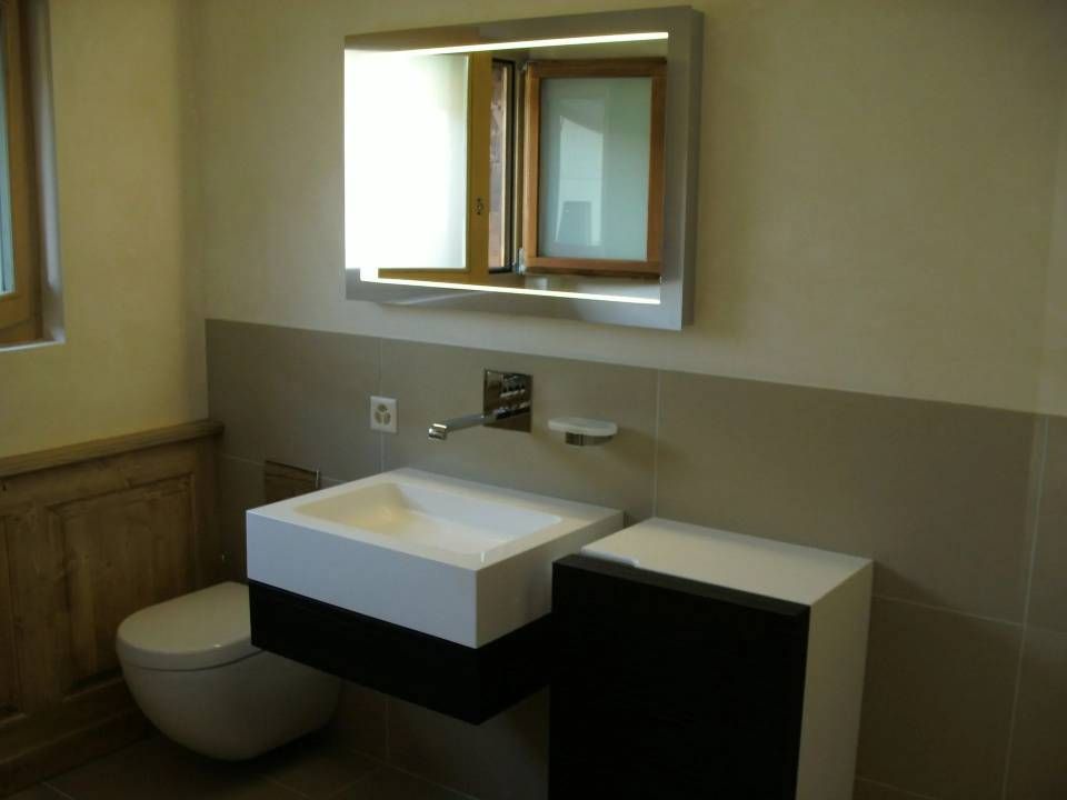 Salle de bains moderne avec lavabo mural, miroir avec éclairage intégré et toilettes.