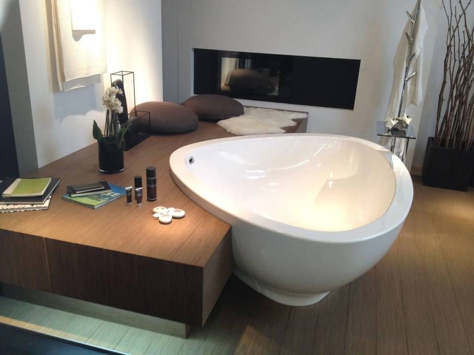 Baignoire blanche moderne intégrée à une plateforme en bois, avec coussins, cheminée et décoration.