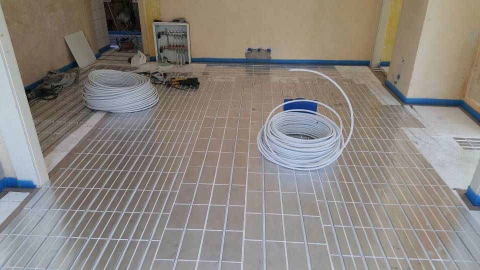 Plancher chauffant avec système de chauffage radiant. Feuille argentée, tuyaux blancs, bordure bleue. Aménagement intérieur.