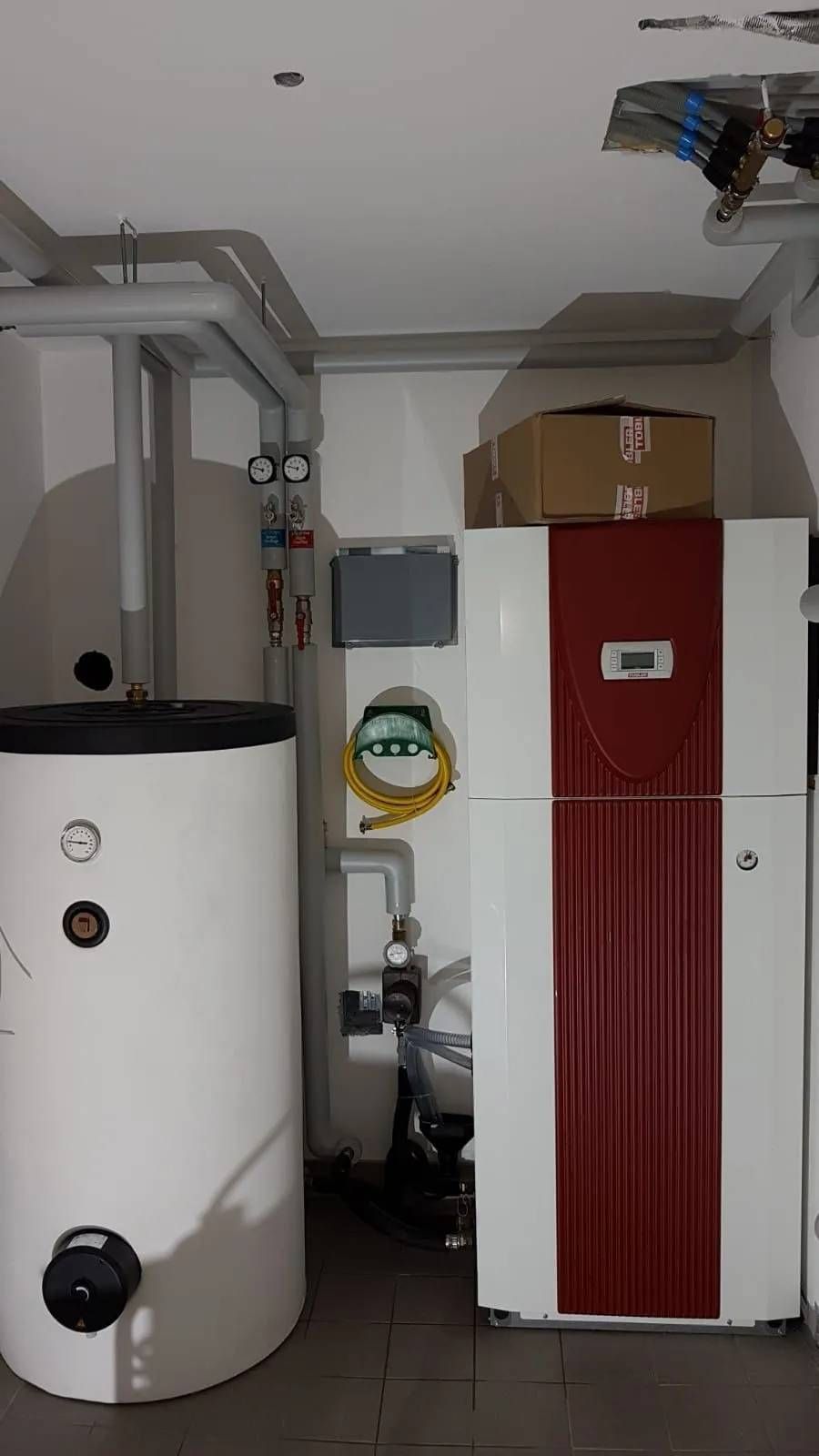 Un système de chauffage blanc et rouge avec un réservoir d'eau blanc dans une buanderie.