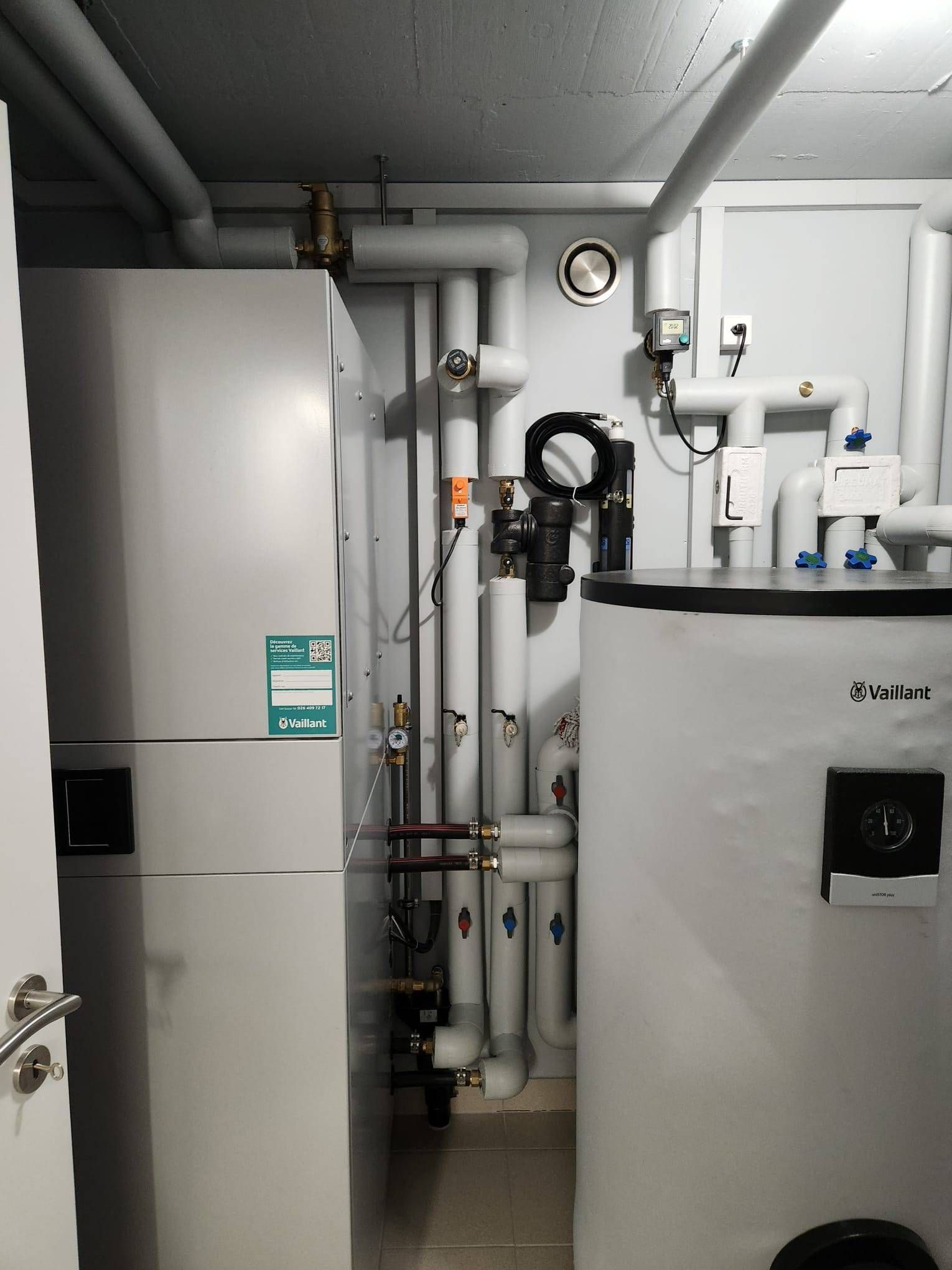 Une buanderie avec pompe à chaleur blanche, chauffe-eau et tuyauterie de raccordement.