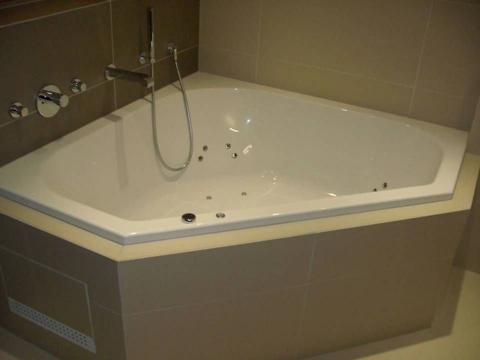 Baignoire jacuzzi d'angle, carrelage beige autour, robinetterie chromée.