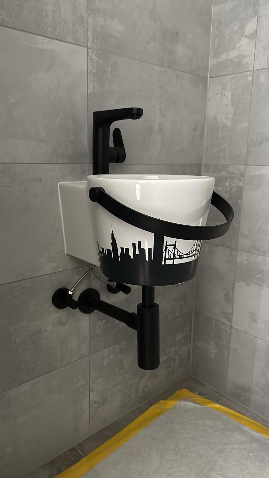 Tuyauterie blanche et en laiton avec robinetterie à poignée bleue, fixée sur un mur blanc dans une buanderie.