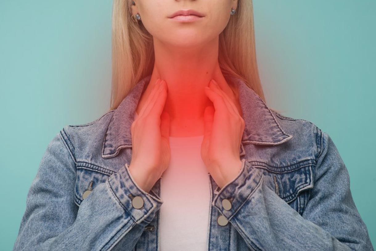 Una mujer se sujeta la garganta con las manos porque le duele la garganta.