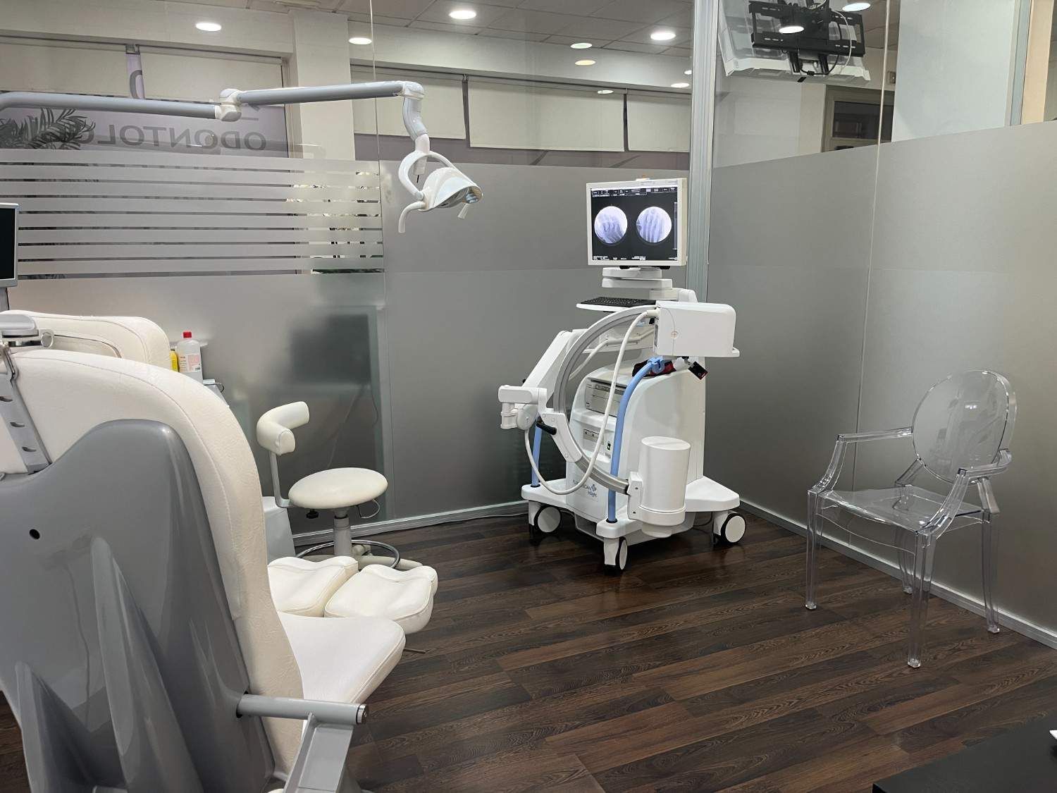 Sala de ecografías del hospital con sillones de exploración, equipo médico y un monitor sobre un suelo de madera oscura.