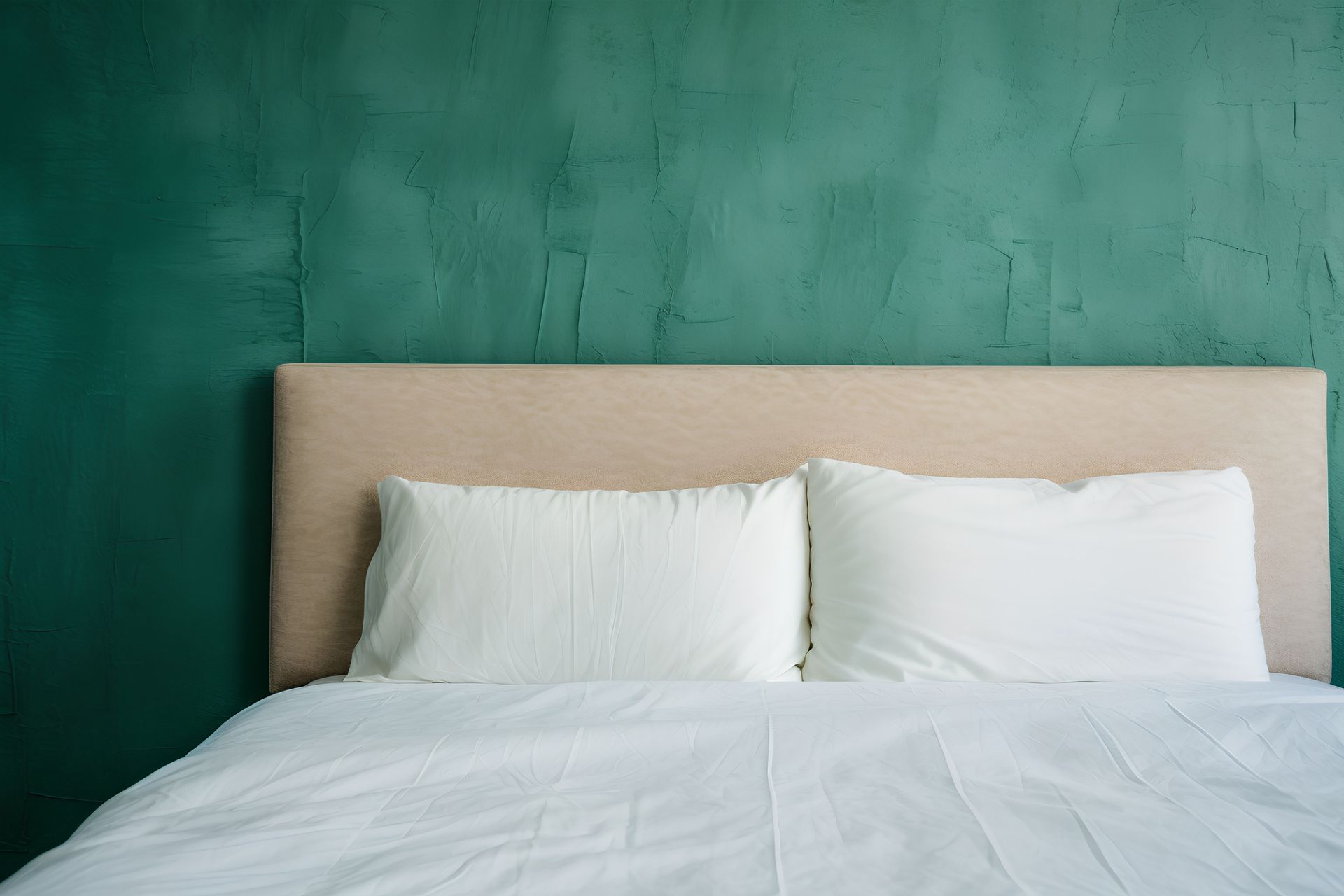 Dormitorio minimalista con cabecero beige, almohadas blancas y pared texturizada verde.
