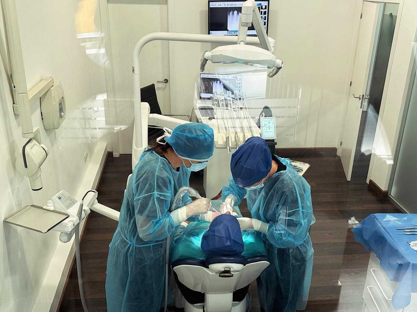 En una clínica dental, unos dentistas con trajes protectores azules realizan un procedimiento a un paciente.