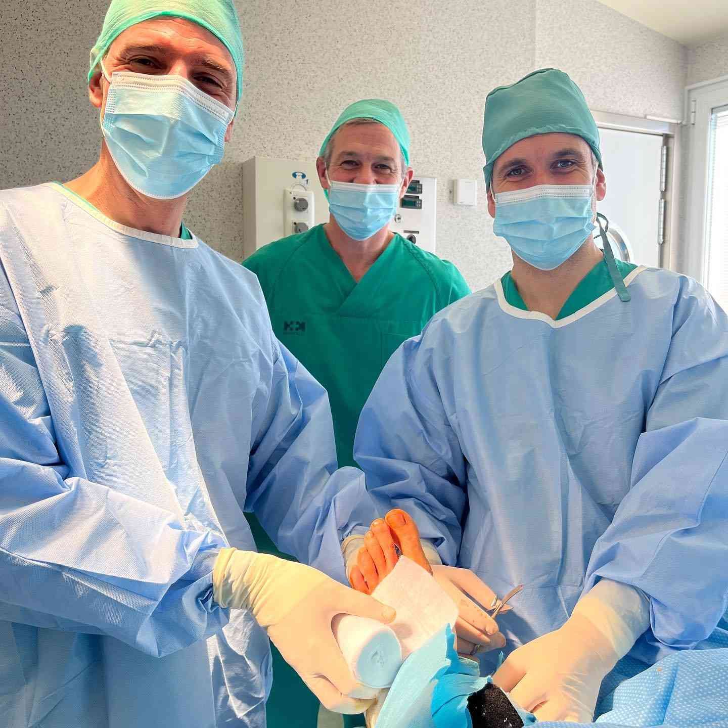 Tres cirujanos enmascarados con uniforme quirúrgico realizan una operación en un quirófano iluminado.