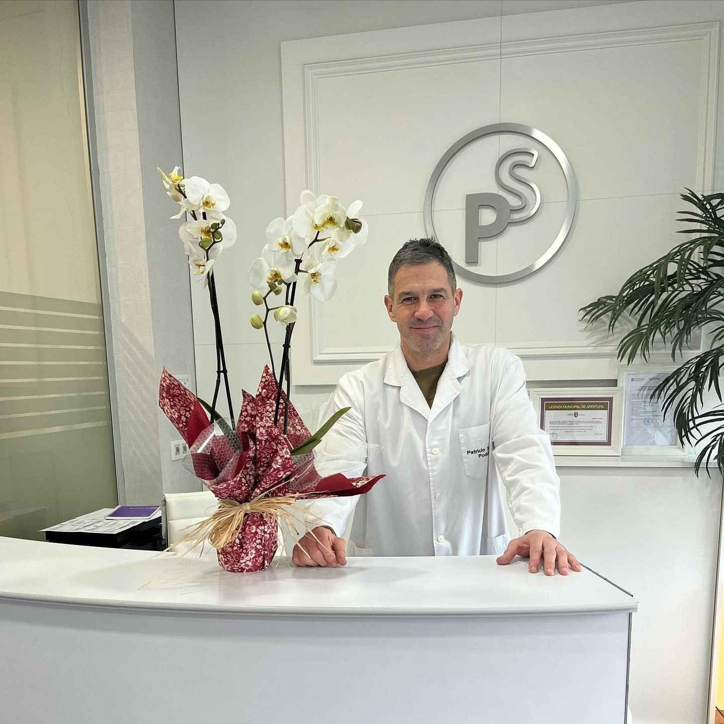 Mostrador de recepción con un hombre con bata blanca y un arreglo floral rojo y blanco.