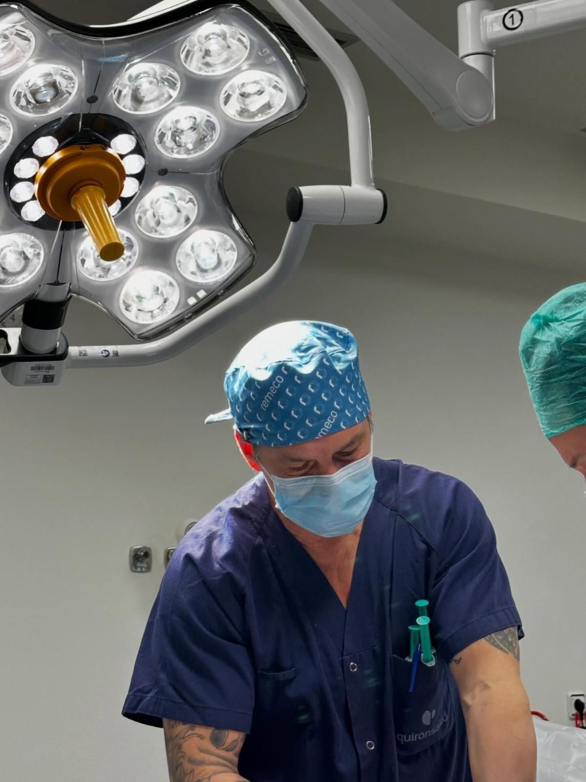 Cirujanos con uniformes azules trabajando bajo la luz de un quirófano durante un procedimiento.