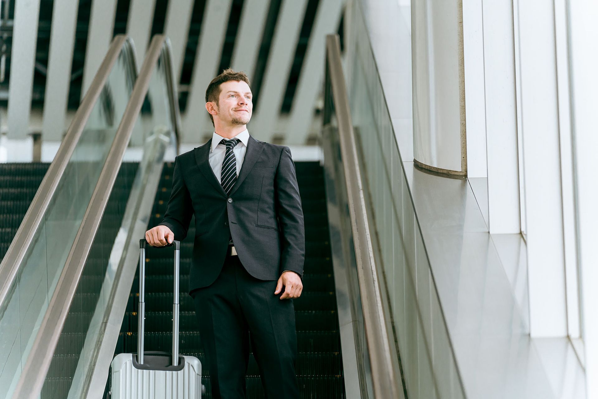 ein Mann in Anzug und Krawatte hält einen Koffer und fährt eine Rolltreppe hinunter