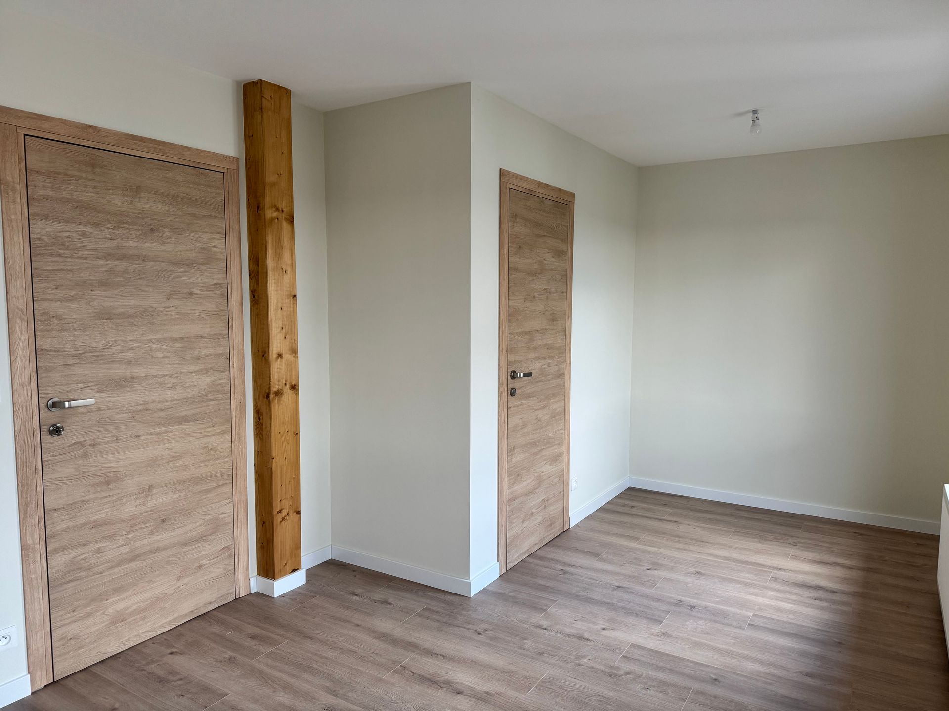 Pièce vide avec murs blancs et portes en bois.
