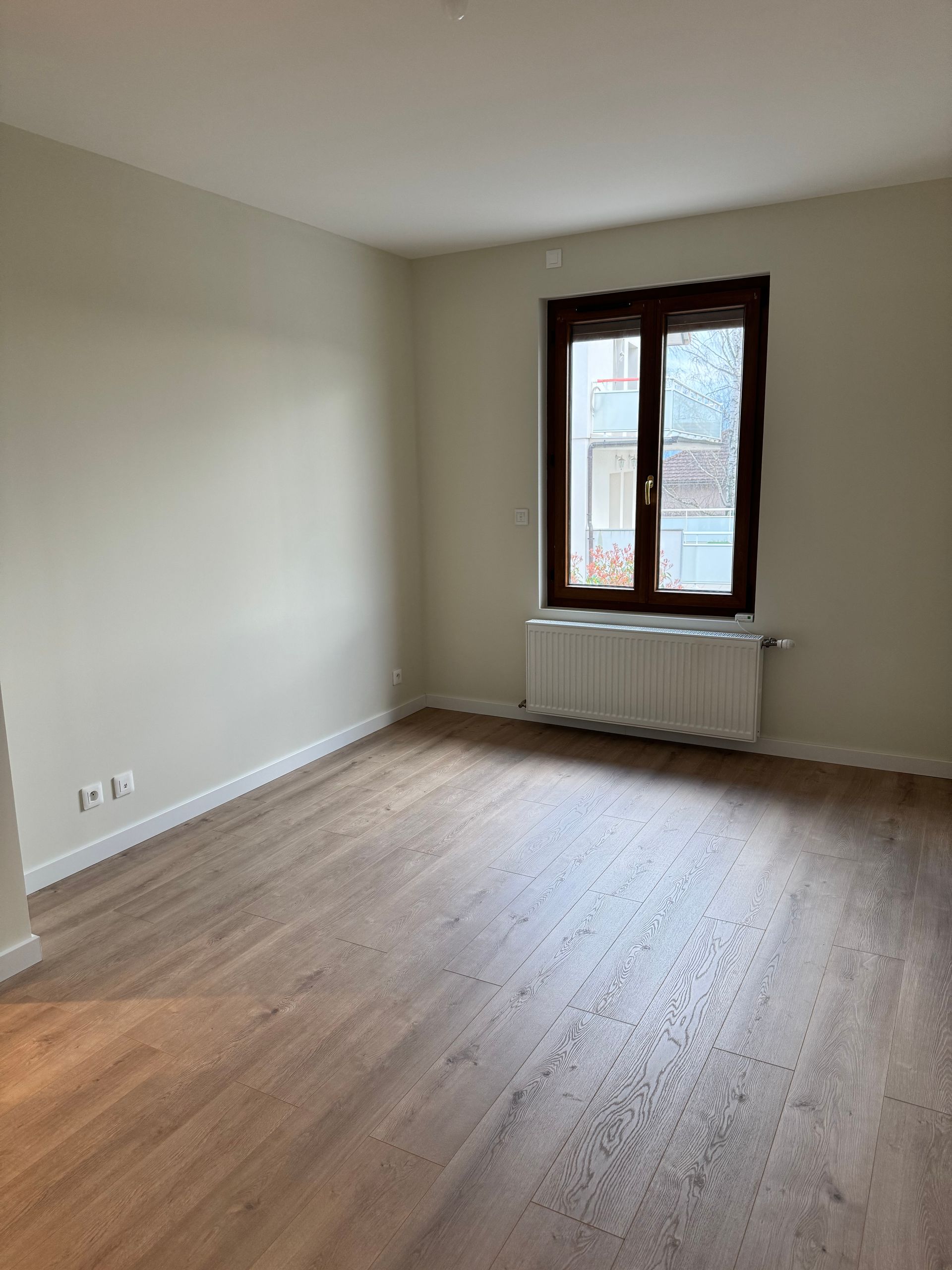 Pièce vide avec parquet et fenêtre aux bords noirs.