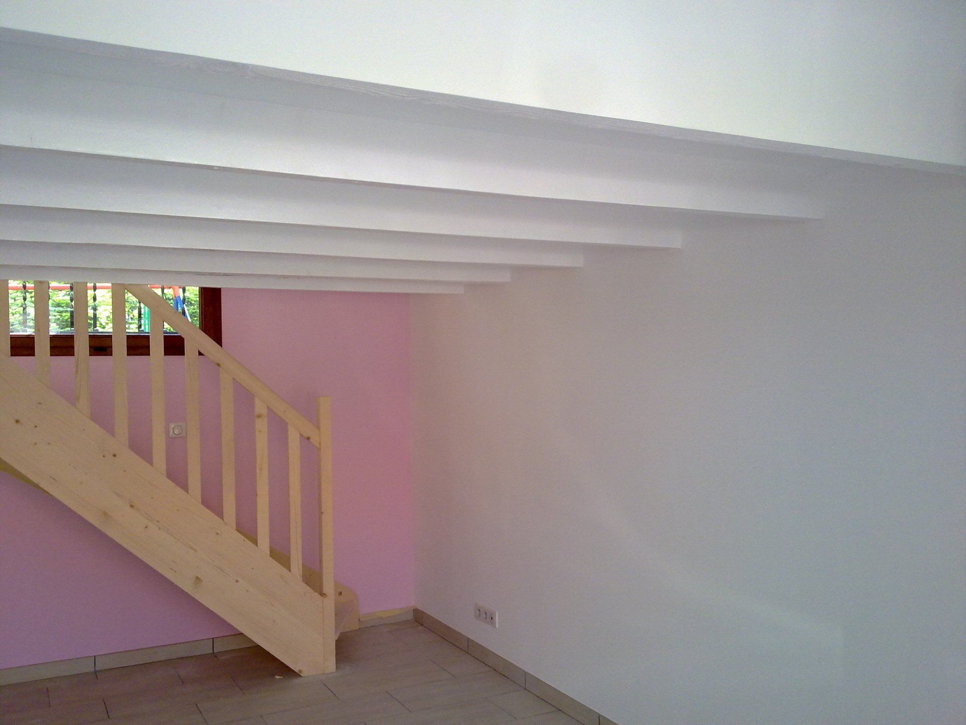 Mur rose d'une pièce avec un escalier en bois.