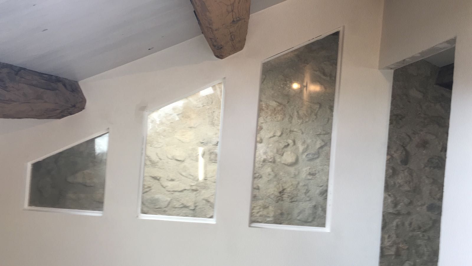 Cloison avec verre donnant sur un mur en pierre sous des combles.