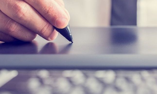 Mano sosteniendo un lápiz óptico, escribiendo en una tableta gráfica digital.