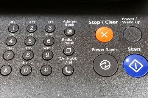 Primer plano de un panel de control de impresora con botones para números, borrar, iniciar, encender y marcar.
