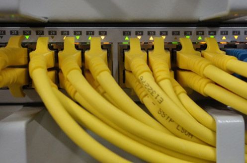 Cables de red amarillos conectados a un conmutador de red con luces de actividad verdes.