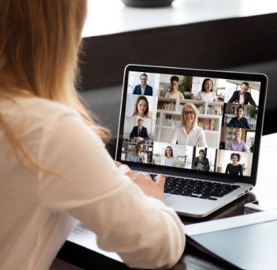 Mujer frente a la pantalla de un ordenador portátil en una videoconferencia con sus compañeros, trabajando desde casa.
