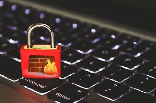 Candado rojo con símbolo de cortafuegos sobre un teclado iluminado, que simboliza la seguridad de la red.