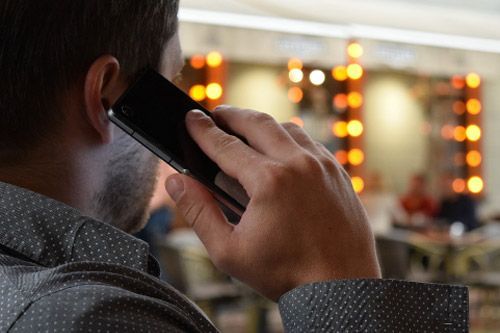 Hombre sosteniendo un teléfono en su oreja, fondo borroso de una habitación muy iluminada.