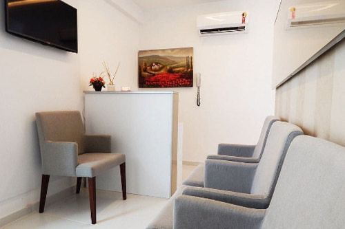 Sala de espera con sillas grises, paredes blancas y un escritorio con un cuadro.