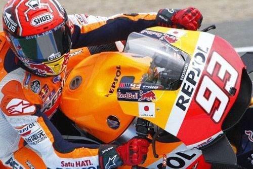 Dos pilotos de motociclismo con monos Repsol naranjas y blancos, cascos tocándose, en la pista.