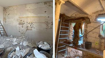 Unfertiges Hausinterieur mit freiliegendem Holzfachwerk, gestapelten Balken und einer teilweise fertiggestellten Küche.