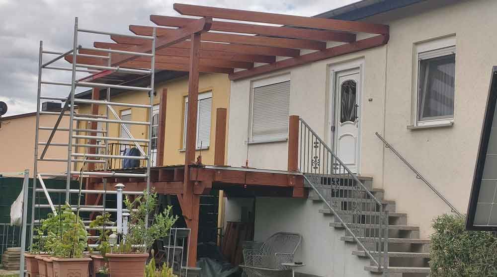 Hausfassade mit Gerüst und einer im Bau befindlichen Holzterrasse neben einer Außentreppe