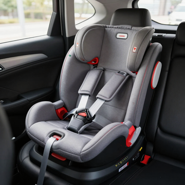 Silla de coche infantil gris con detalles rojos instalada en el asiento trasero de un coche.