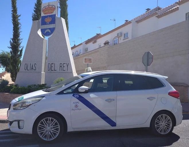 Un coche blanco aparcado junto a un cartel que decía “Olas del Rey” en una calle soleada.