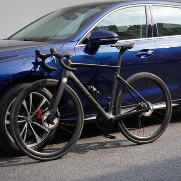 Dos bicicletas de carretera aparcadas delante de un coche azul en una calle.