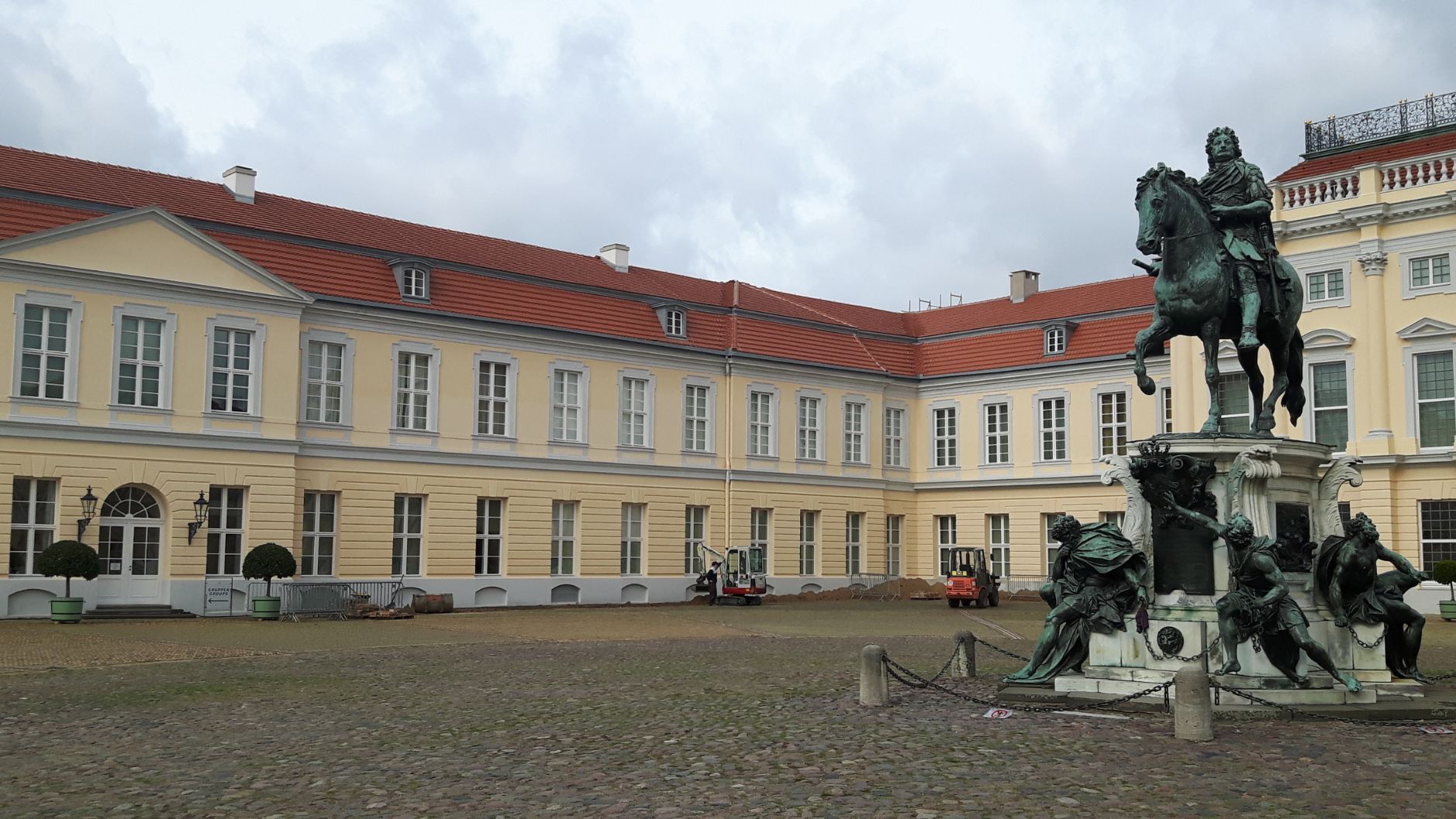 längliches Gebäude mit rotem Dach und Statue auf dem Hof