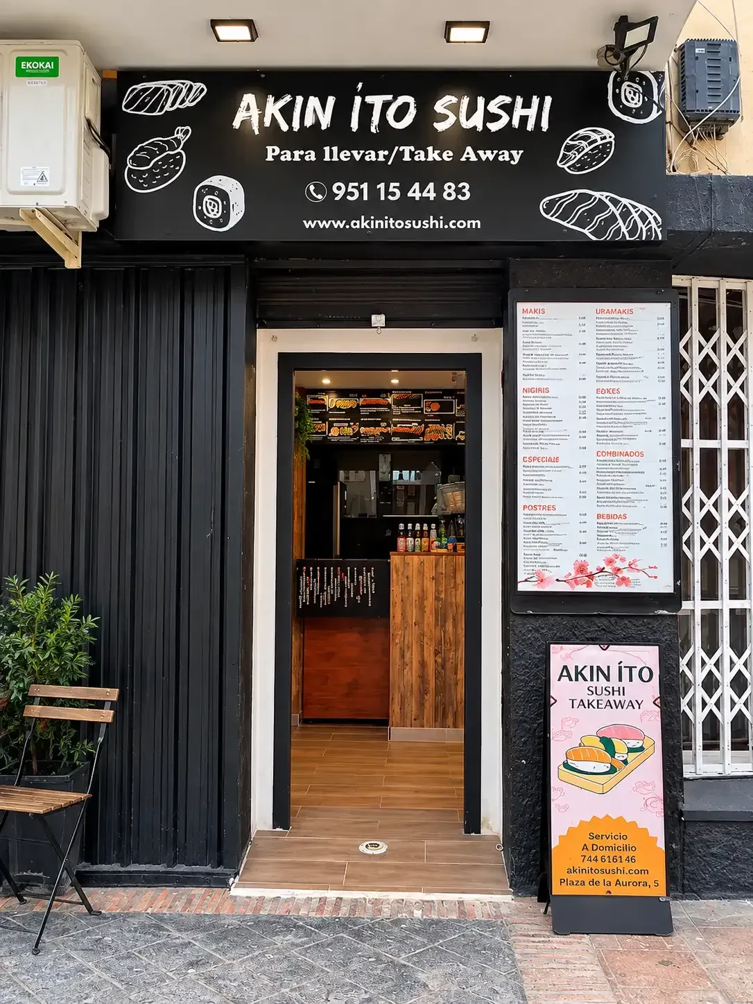 Fachada de restaurante de sushi con fachada negra, puerta de madera, pizarras con el menú y entrada desde la acera.