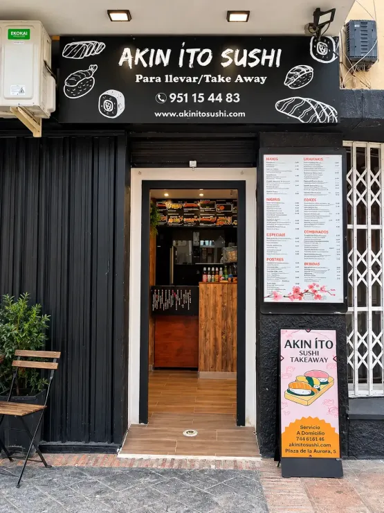 Fachada de restaurante de sushi con fachada negra, puerta de madera, pizarras con el menú y entrada desde la acera.