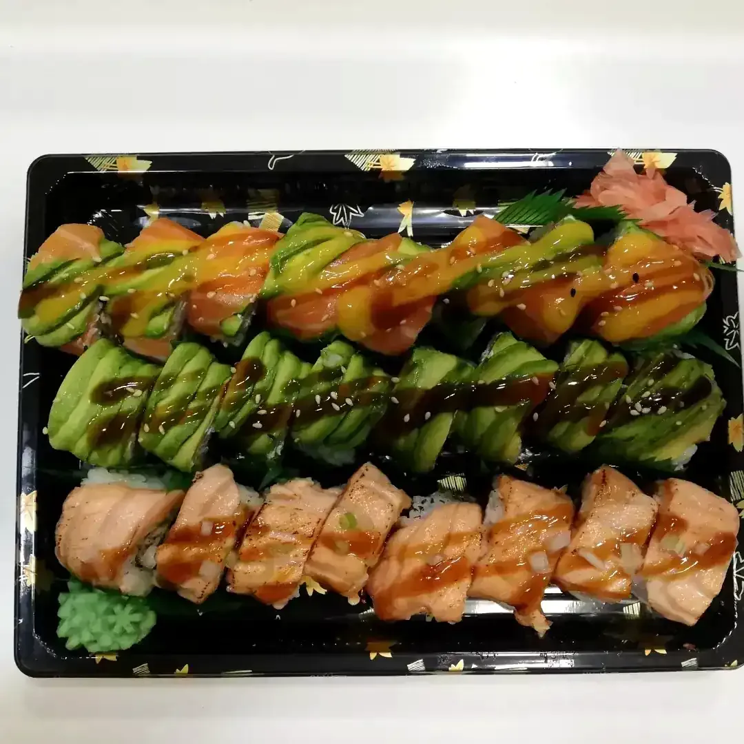 Surtido de rollos de sushi en una bandeja negra, cubiertos con aguacate, salmón y salsa.