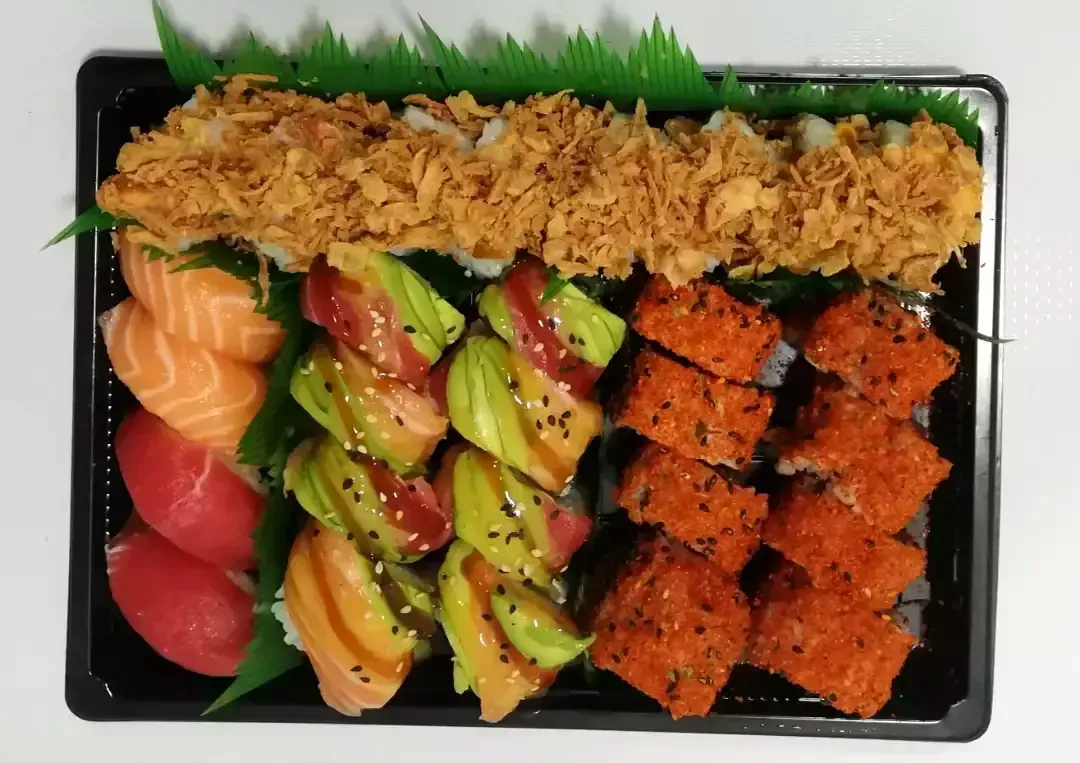 Caja bento de sushi variado con rollos de salmón, atún y aguacate, y una cobertura crujiente frita.