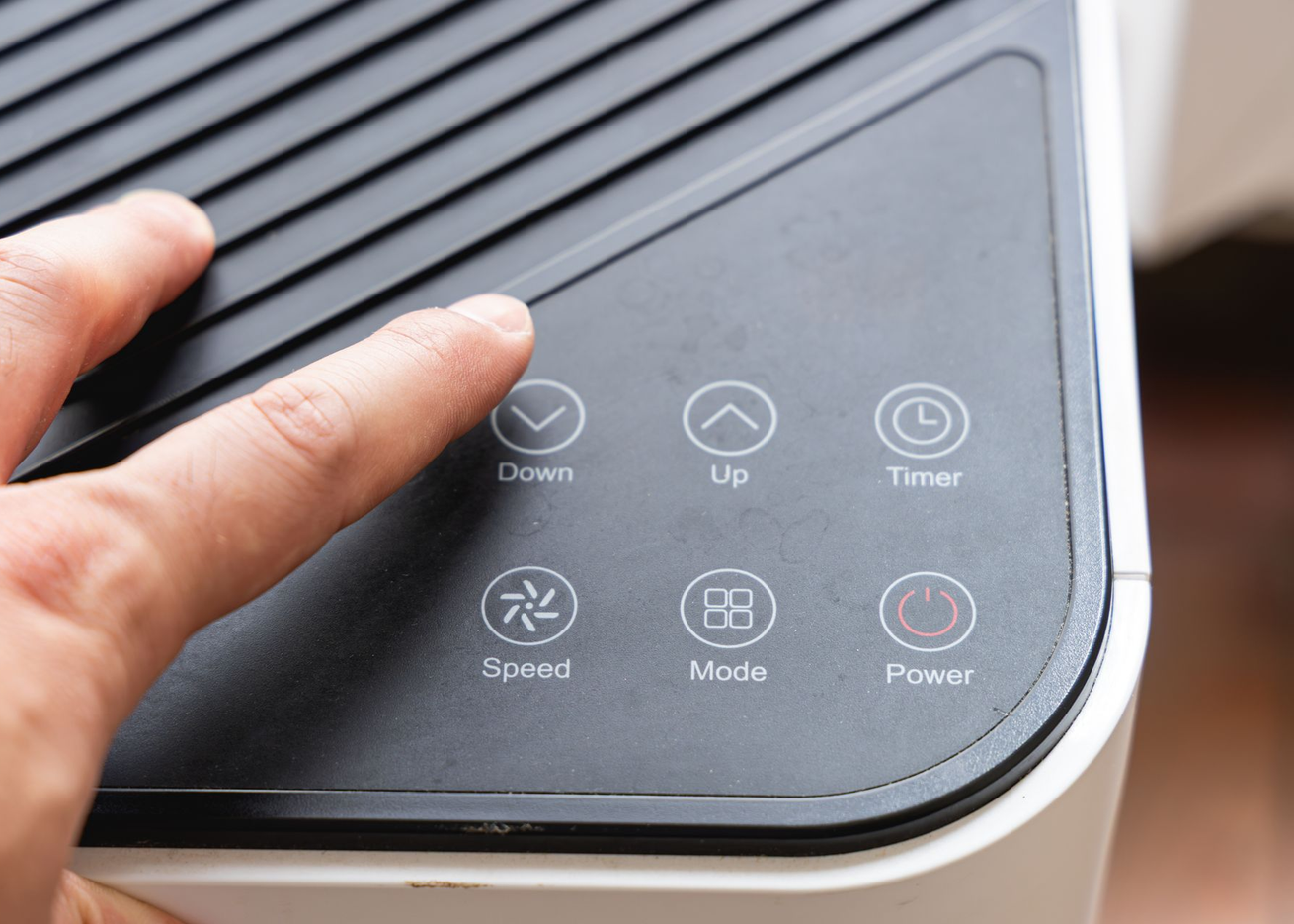 Le doigt d'une personne appuie sur le bouton « Bas » sur un panneau de commande de purificateur d'air noir avec divers réglages.