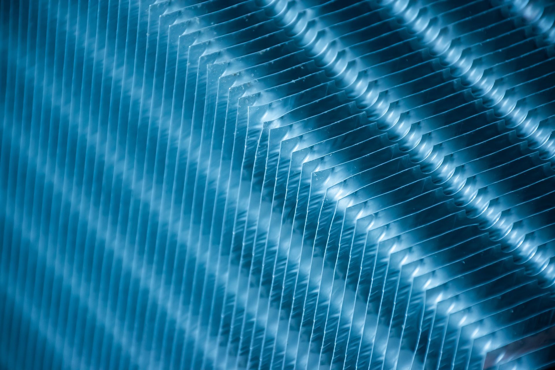 Gros plan aux tons bleus des ailettes d'un radiateur, disposées en diagonale, créant un motif répétitif de lumière et d'ombre.