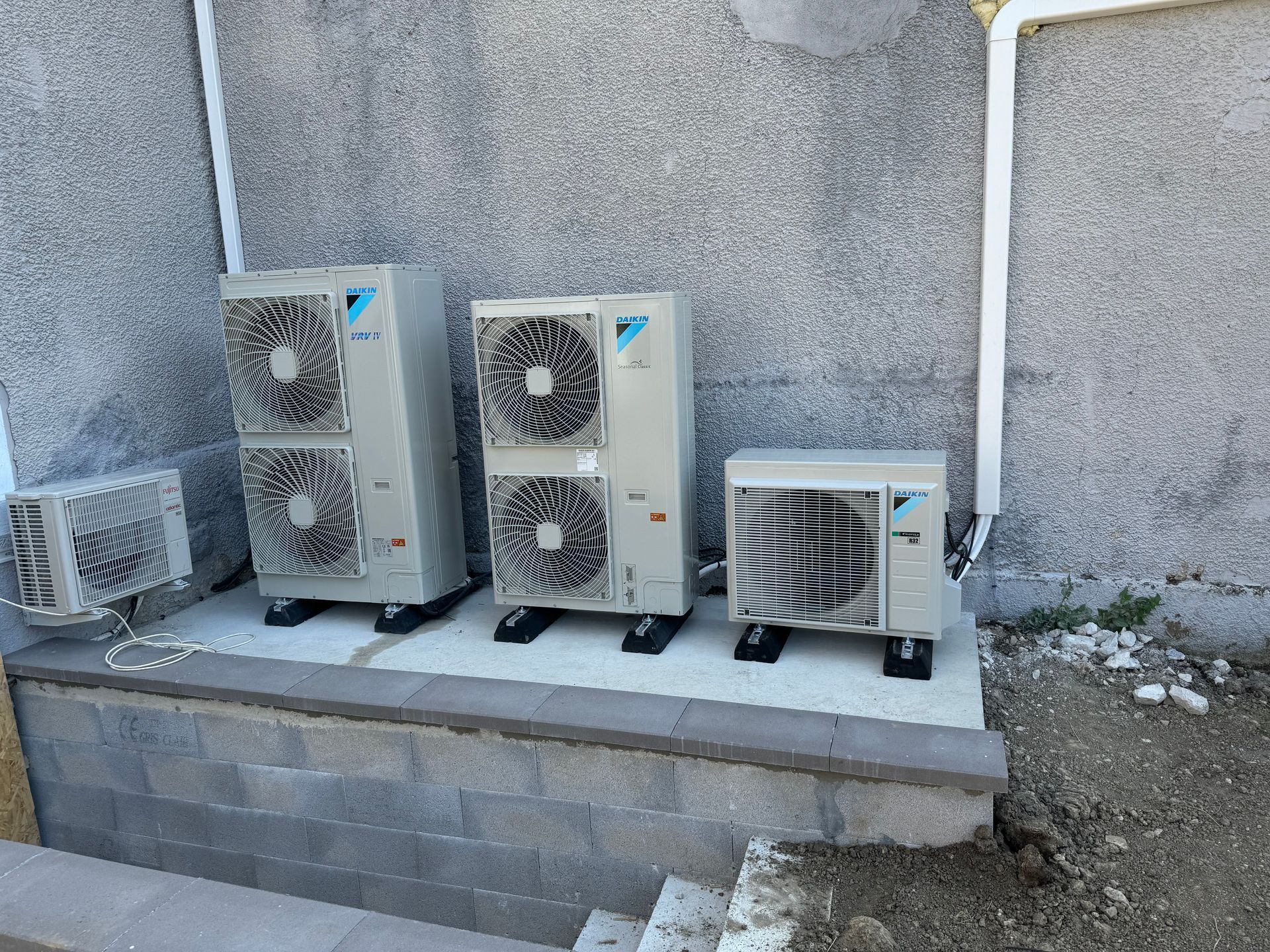 Quatre unités CVC Daikin sur une plate-forme en béton contre un mur en stuc gris.