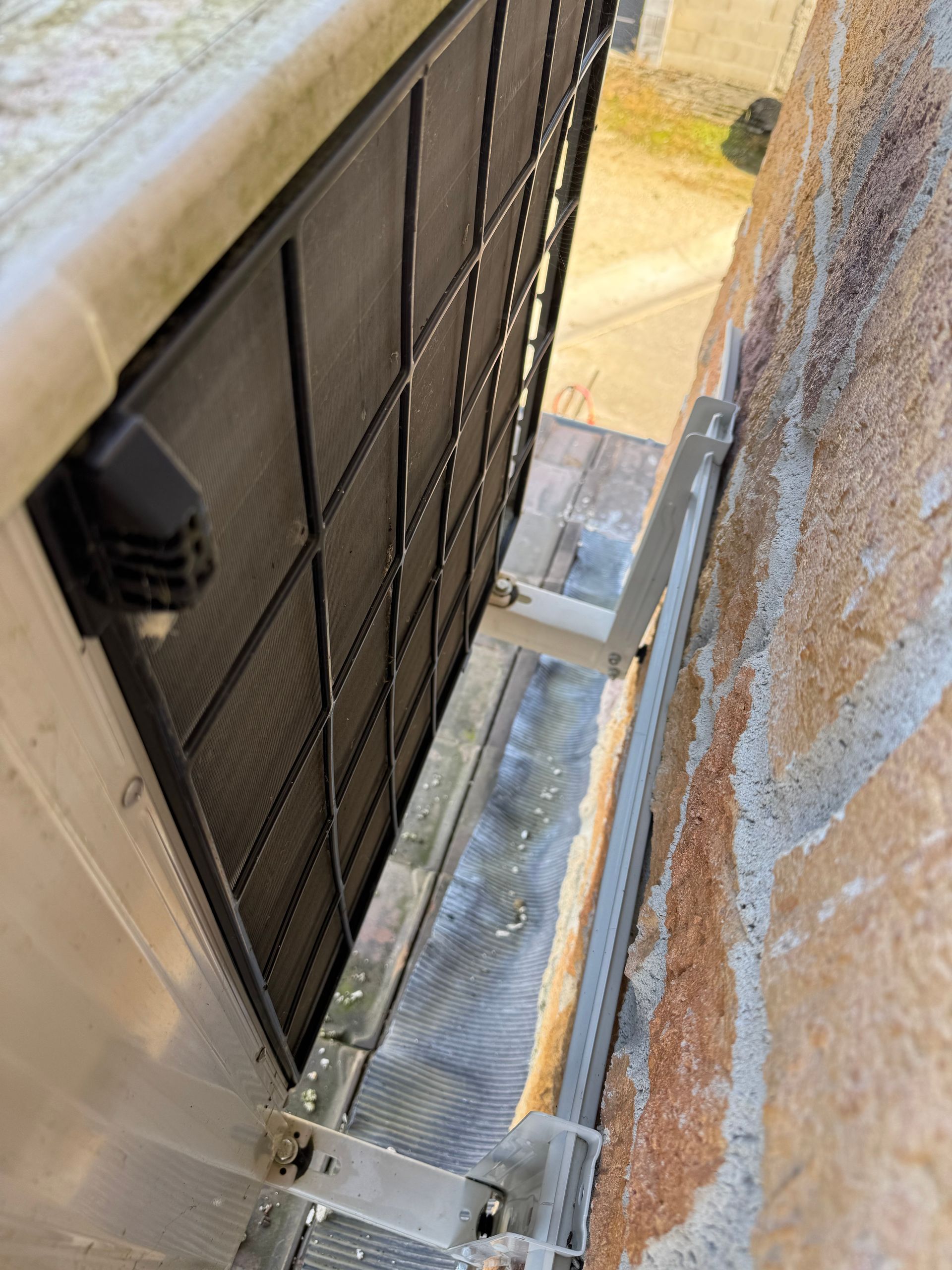 Écran métallique sur un bâtiment, entre un mur et une gouttière, vu de dessus.