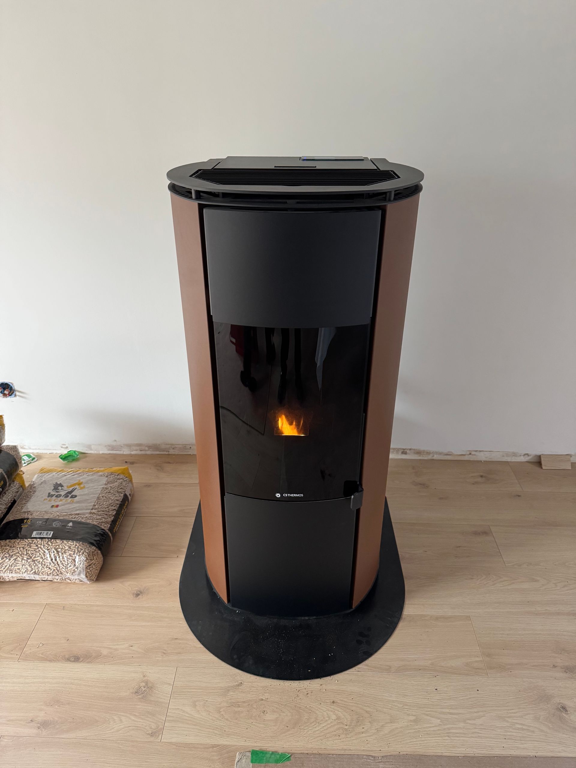 Un poêle à granulés marron et noir avec une flamme visible, sur un plancher en bois.