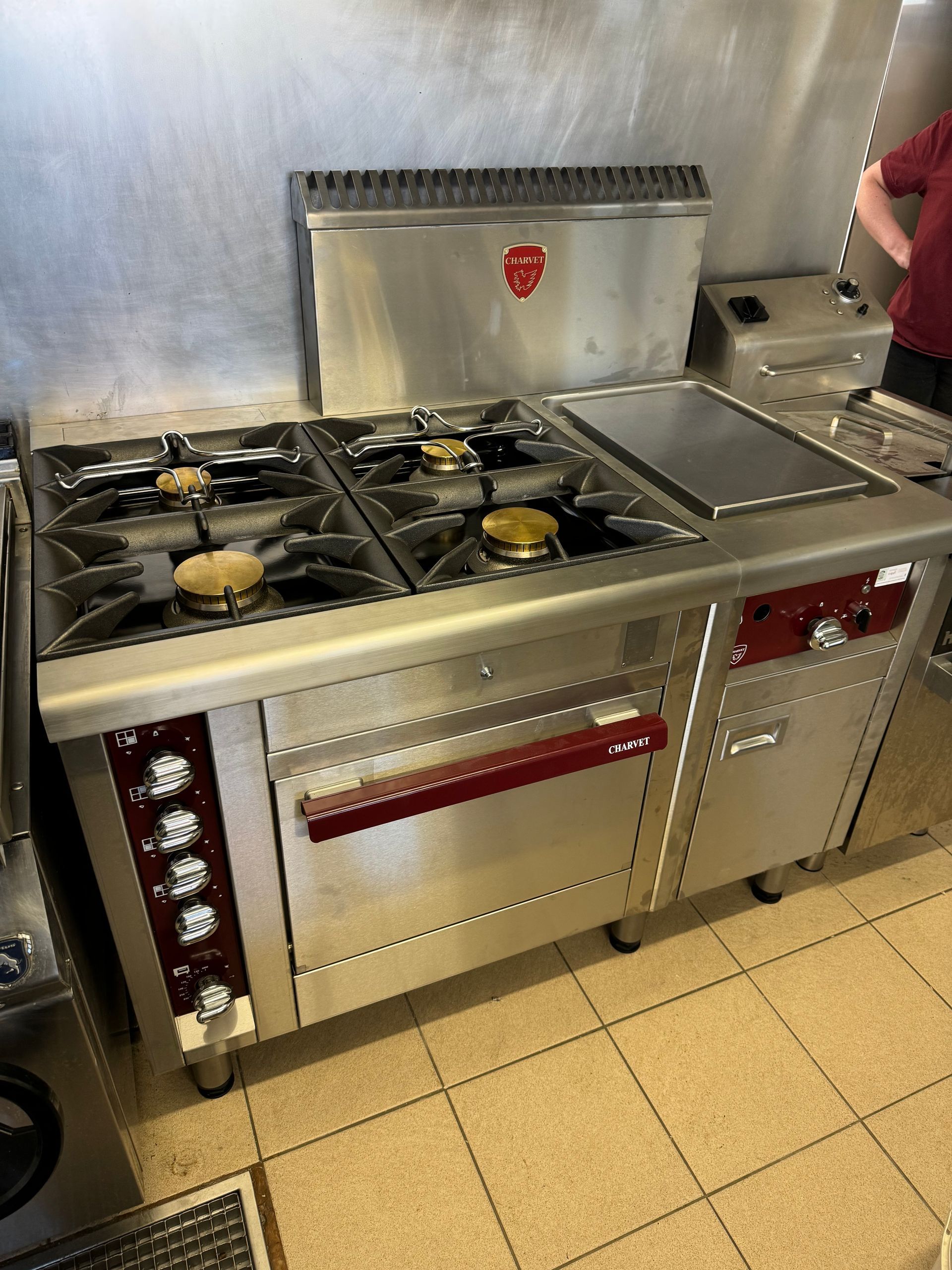 Cuisinière à gaz commerciale en acier inoxydable avec six brûleurs, plaque chauffante et four dans une cuisine.