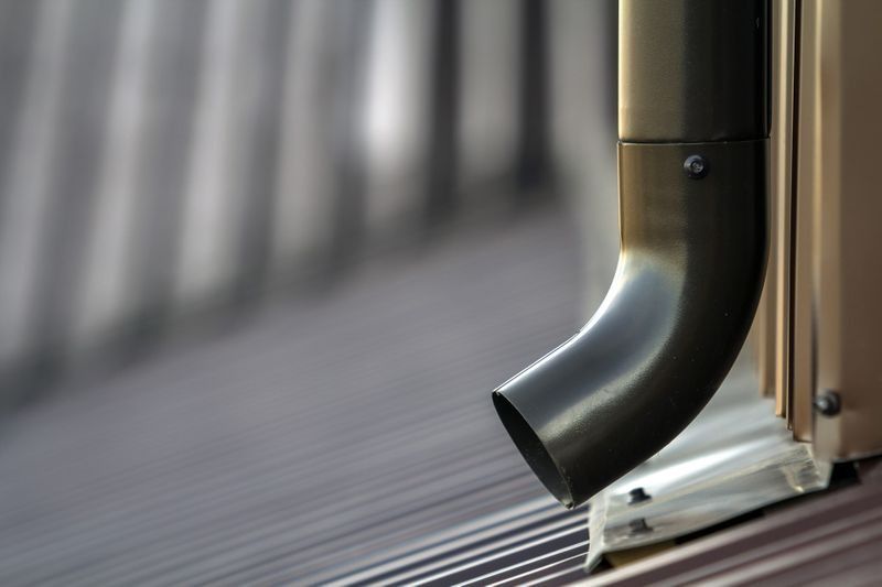 Tumma syöksytorvi rakennuksen aaltopeltikatolla, kulmassa katsojaa kohti.