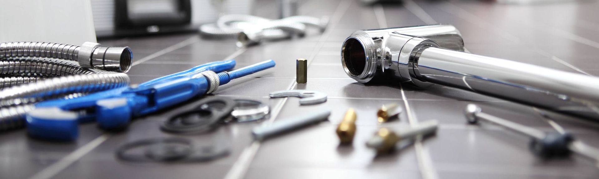 Laatoitetulle pinnalle järjestettyjä putkityökaluja ja -osia, mukaan lukien kromiputket, sininen työkalu ja pieniä liittimiä.