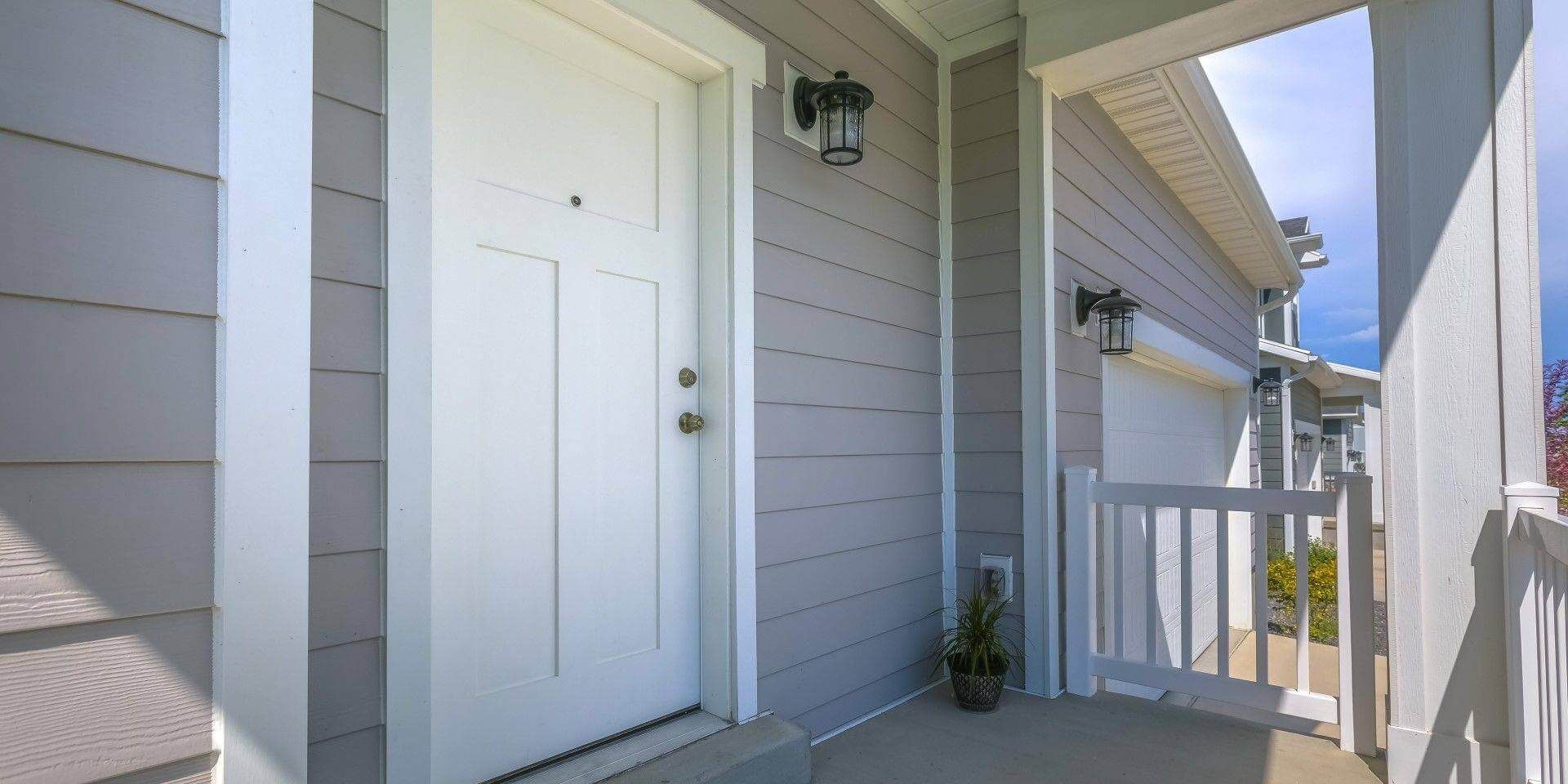 Valkoinen etuovi harmaassa talossa, jossa on pieni kuisti ja valkoiset listat.